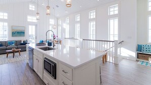 Una cocina amplia con una isla grande, muebles blancos y lámparas colgantes.