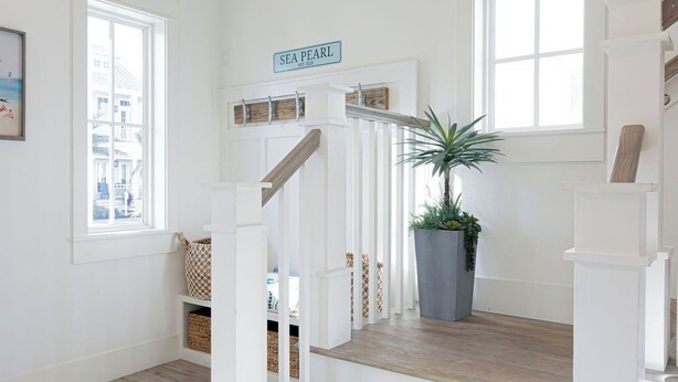 Una escalera con barandillas blancas y acabado de madera, que conduce a una plataforma con una planta en maceta y un letrero que dice "SEA PEARL".