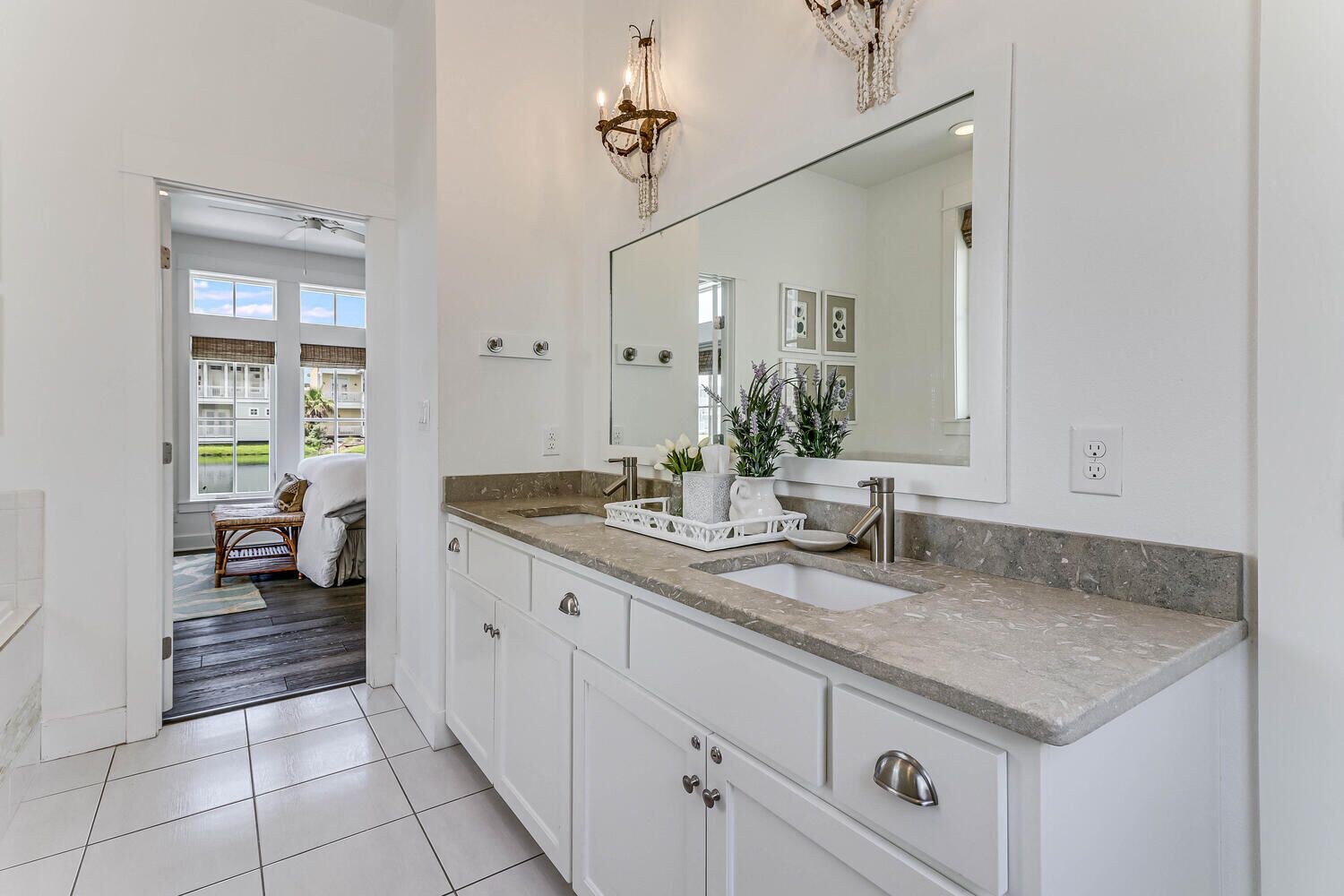 A modern bathroom with a large mirror, white cabinetry, and a marble countertop.