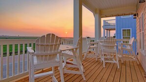 Une terrasse en bois avec des fauteuils Adirondack, une table et une vue sur le coucher de soleil sur l’océan.
