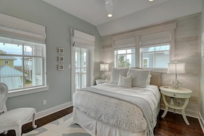 A bedroom with a bed, two bedside tables, a chair, and windows with blinds.