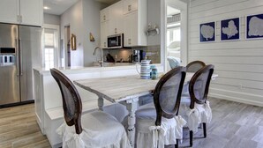 A modern kitchen with white cabinetry, a central island, and a dining area with four chairs. - So Long TC 10305 (Port Aransas)