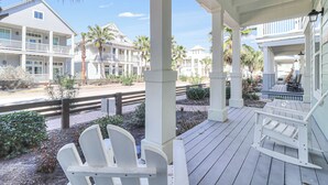 A covered porch with white Adirondack chairs, a wooden deck, and a view of beachfront properties. - Shore Magic 116 ST (Port Aransas)