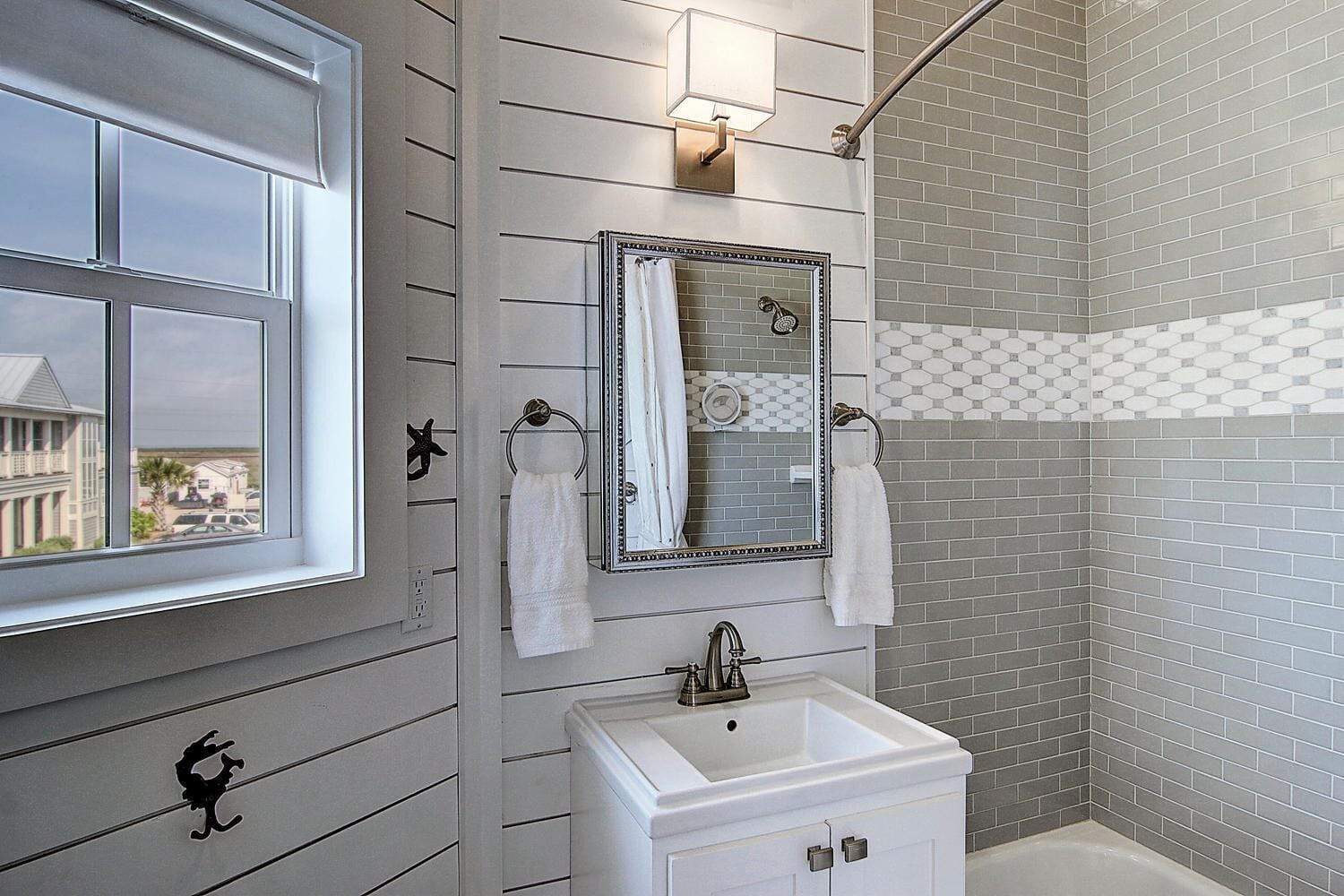 A bathroom with a window, a sink, a mirror, and a shower area.