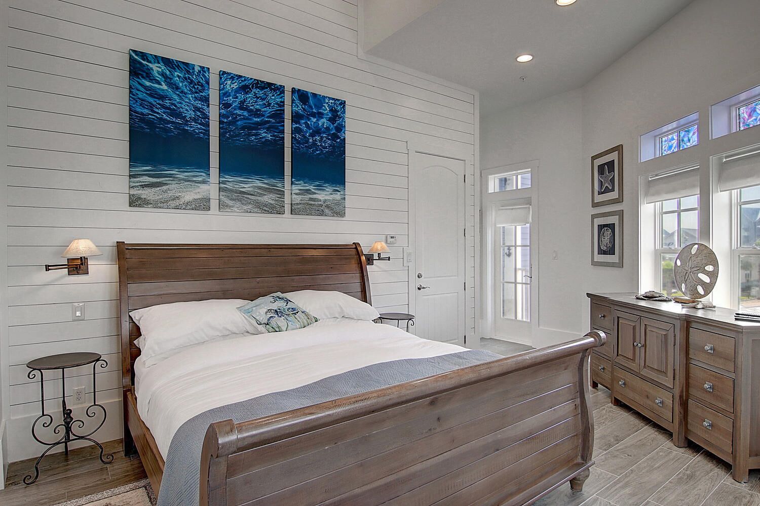 A bedroom with a wooden bed, a nightstand, a dresser, and a large window.
