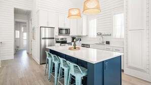 A modern kitchen with white cabinetry, a central island with bar stools, stainless steel appliances, and pendant lighting.