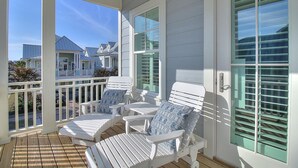 Une véranda couverte avec des fauteuils Adirondack blancs et une terrasse en bois.
