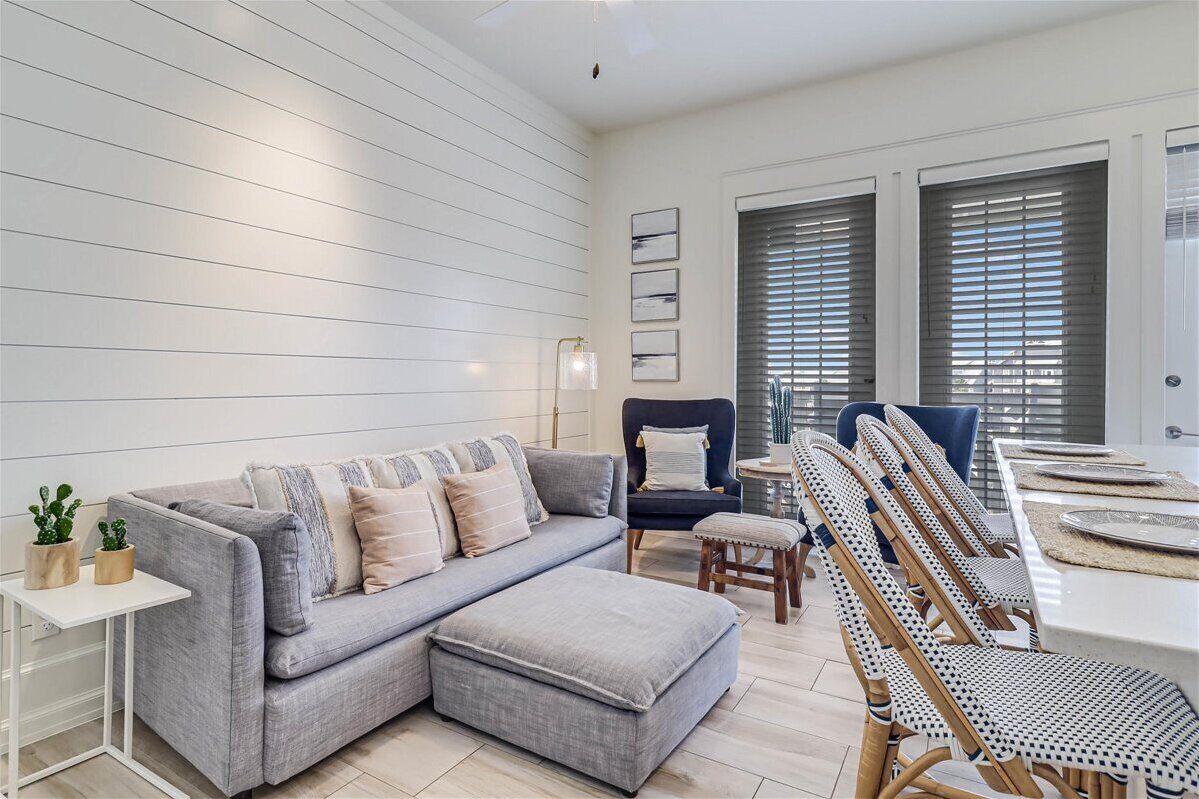 A modern living room with a grey sectional sofa, a small white table, wicker chairs, and a dining area with a white table and chairs.