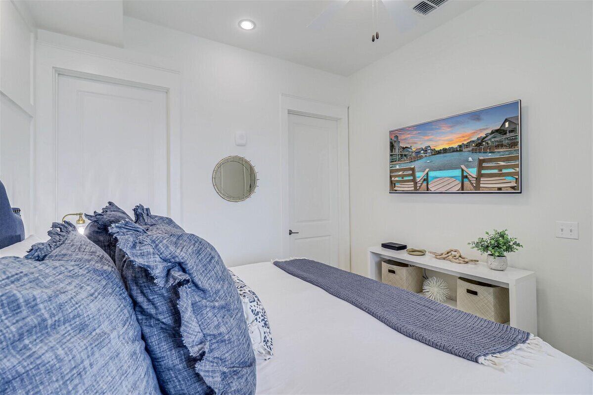 A bedroom with a bed, a bedside table, a mirror, and a painting of a waterfront scene.