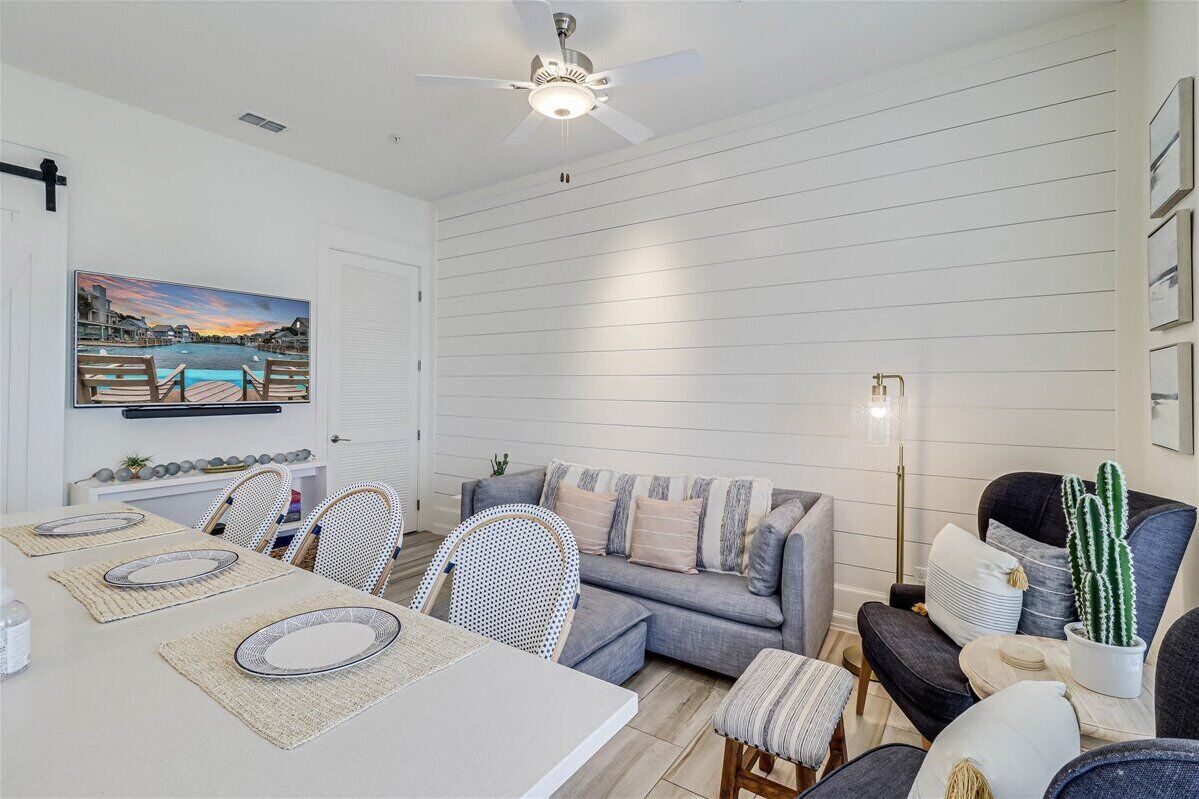 A modern living room with a dining area, featuring a ceiling fan, a painting of a sunset, and a cactus plant.