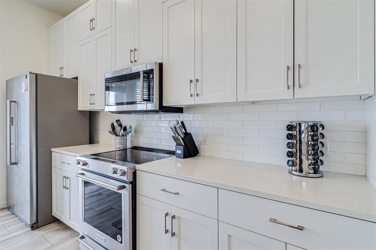A modern kitchen with white cabinets, a stainless steel refrigerator, a microwave, an oven, and a knife block.