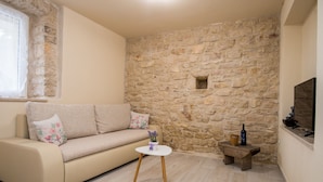 Un salon chaleureux avec un canapé beige, une petite table ronde et un mur en pierre.