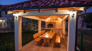 Une terrasse extérieure dotée d’une cheminée en briques, de bancs en bois et d’une pergola illuminée.
