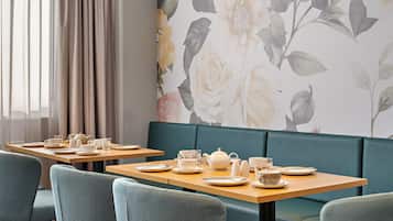 En restaurant med træborde, grønne polstrede bænke og blomstret tapet.