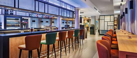 Een bar met een lange toonbank, meerdere krukken en een zithoek met tafels en stoelen.