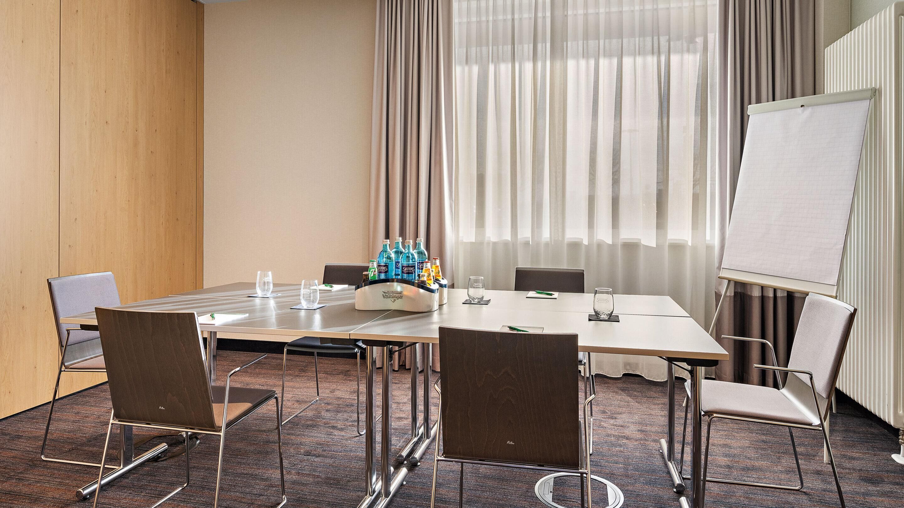A conference room with a large table, chairs, a whiteboard, and a window with curtains.
