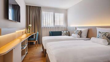 Een hotelkamer met twee bedden, een bureau, een stoel en een groot raam met gordijnen.