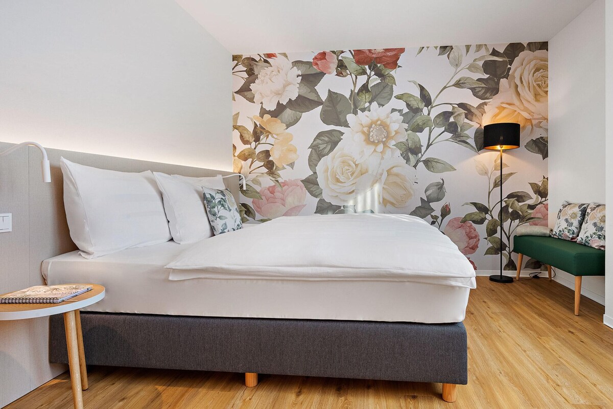 A bedroom with a bed, bedside table, lamp, and a green bench.