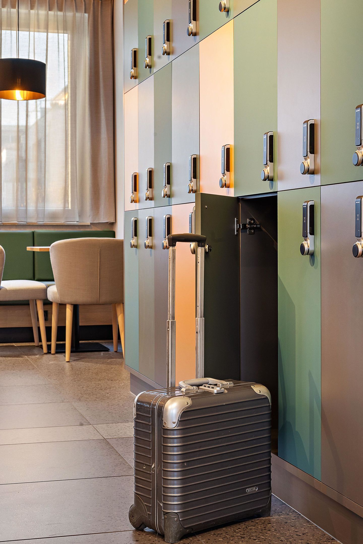 Une chambre d’hôtel avec une valise, un coin repas avec une table et des chaises, et une rangée de casiers.