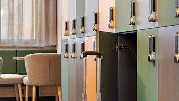 Une chambre d’hôtel avec une valise, un coin repas avec une table et des chaises, et une rangée de casiers.