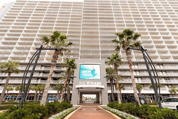 Un hôtel à plusieurs étages, doté d’une entrée principale, de palmiers et d’une enseigne indiquant « THE WHARF ».
