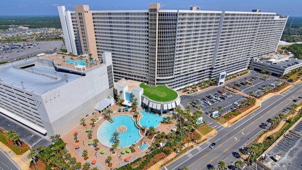 A large hotel with multiple floors, a central courtyard with a swimming pool, and a parking area.