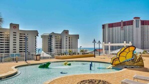 A hotel pool area with a butterfly sculpture, a clear sky, and high-rise buildings in the background.