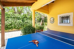 A blue ping pong table with paddles and balls, a yellow wall with a window, and a wooden pergola structure. - Getaway w/ heatable pool and jacuzzi in Albufeira (Albufeira)