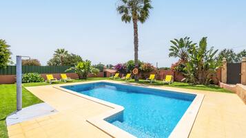 A rectangular swimming pool with a tiled border, surrounded by a paved deck.