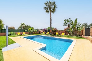 Una piscina rectangular amb un marc de rajoles, envoltada per un solàrium pavimentat.