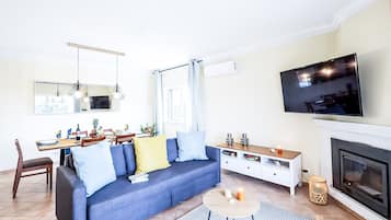 Una sala moderna con sofá, mesa de comedor, televisor, chimenea y elementos decorativos.