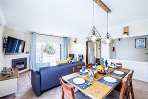 Un saló modern amb un sofà, una taula de dinar preparada per a quatre persones i un televisor fixat a la paret.
