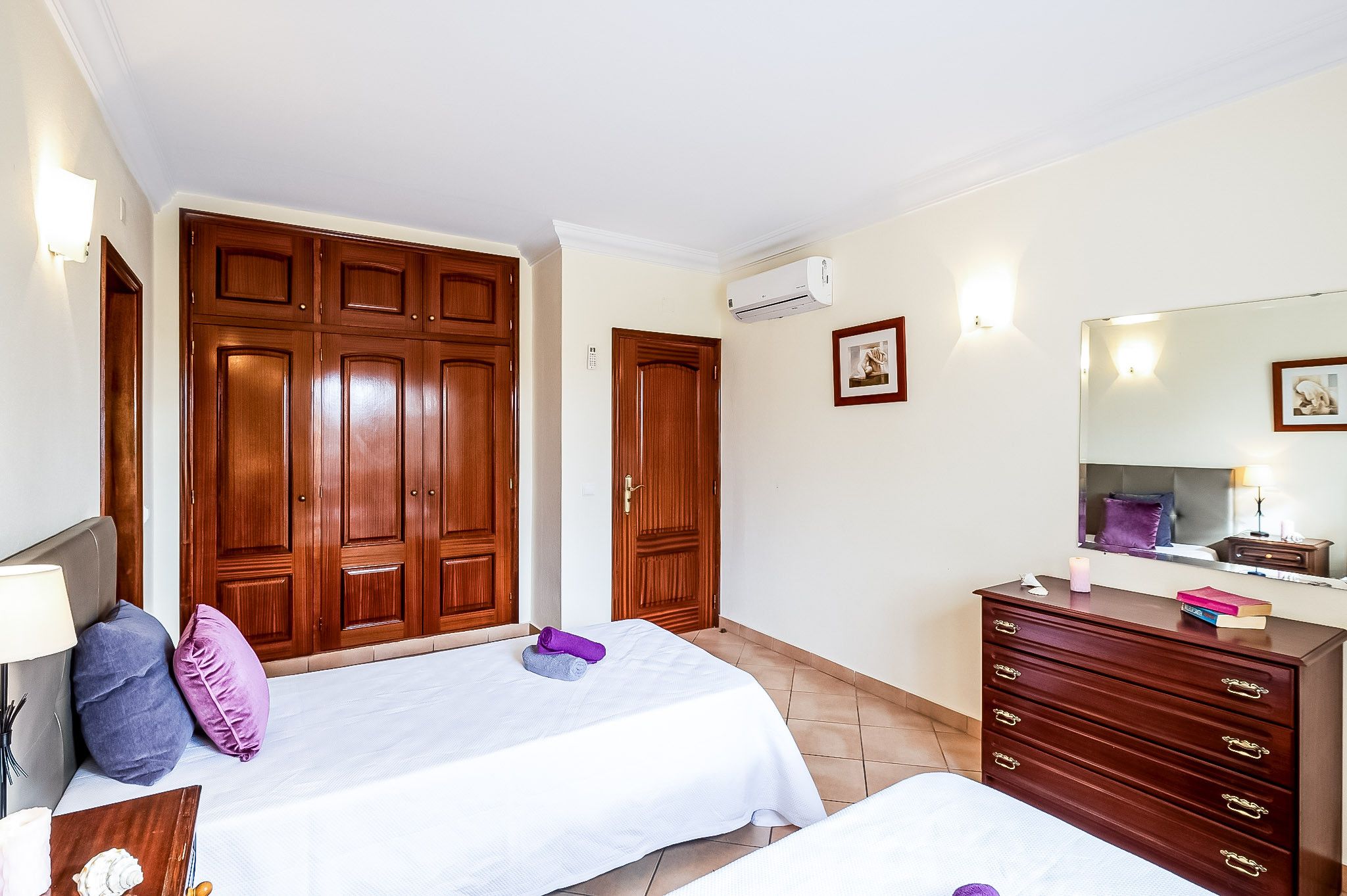 A hotel room with two beds, a dresser, a mirror, and a wardrobe.