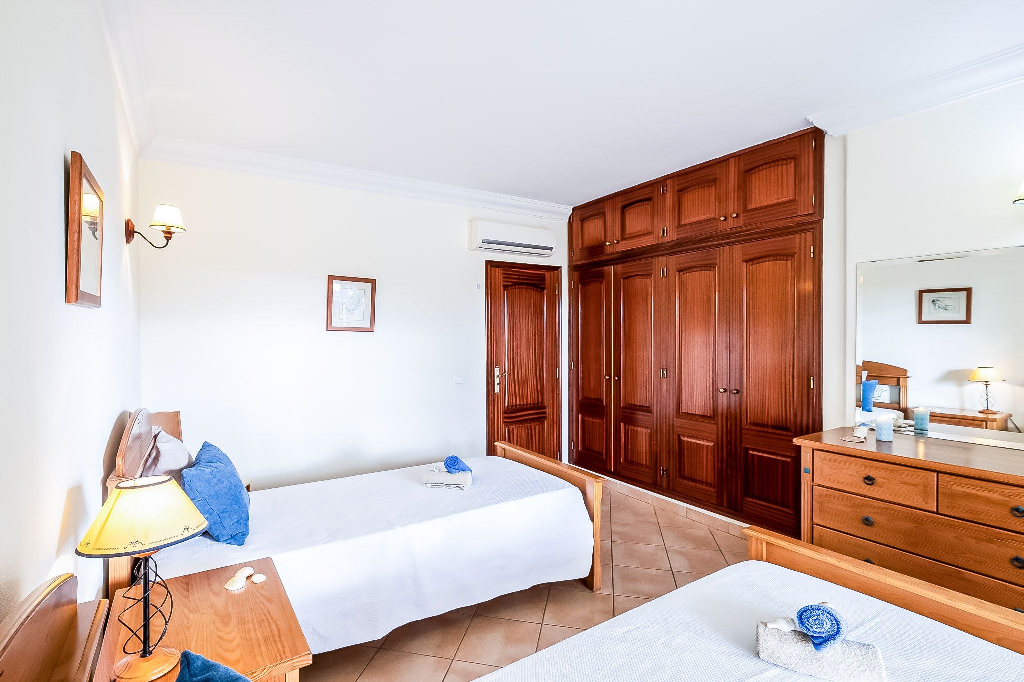 Habitación de hotel con dos camas, un armario de madera, un escritorio con lámpara y la puerta del baño.