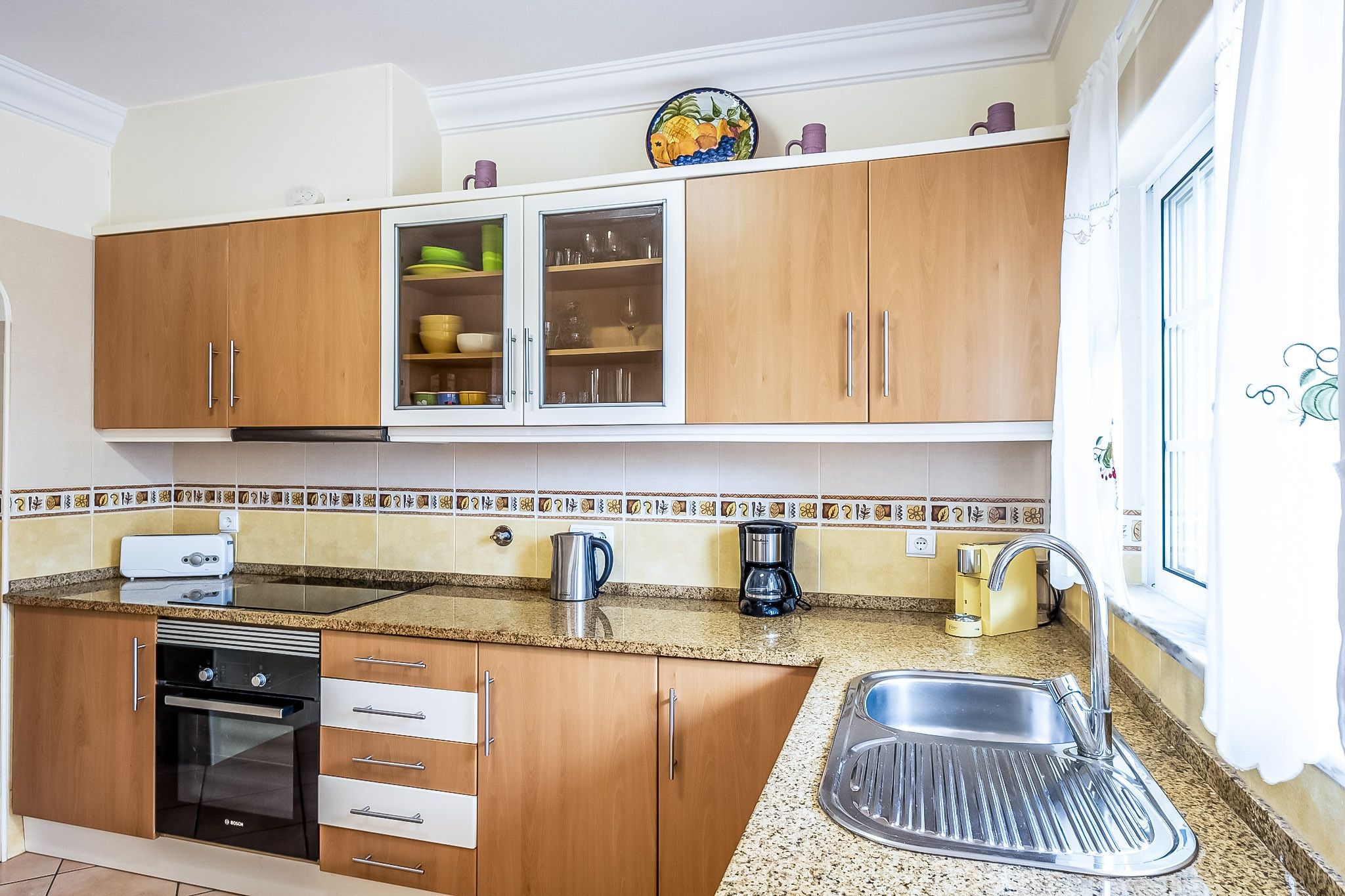 Cocina con armarios de madera, pileta de acero inoxidable, cafetera y tostadora.