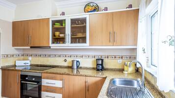 Cocina con armarios de madera, pileta de acero inoxidable, cafetera y tostadora.