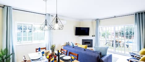 A modern living room with a dining area, a sofa set, and a TV mounted on the wall.