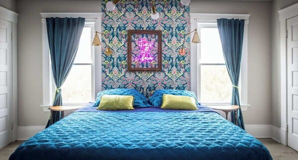 A bedroom with a bed, two bedside tables, a neon sign, and a patterned wallpaper.