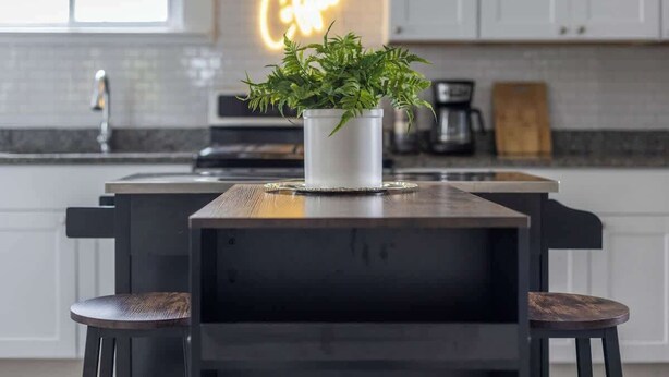 A modern kitchen with a central island, a neon sign, and a potted plant.