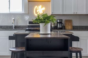 A modern kitchen with a central island, a neon sign, and a potted plant.