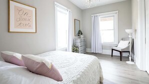 A bedroom with a bed, a dresser, a chair, and a chandelier.