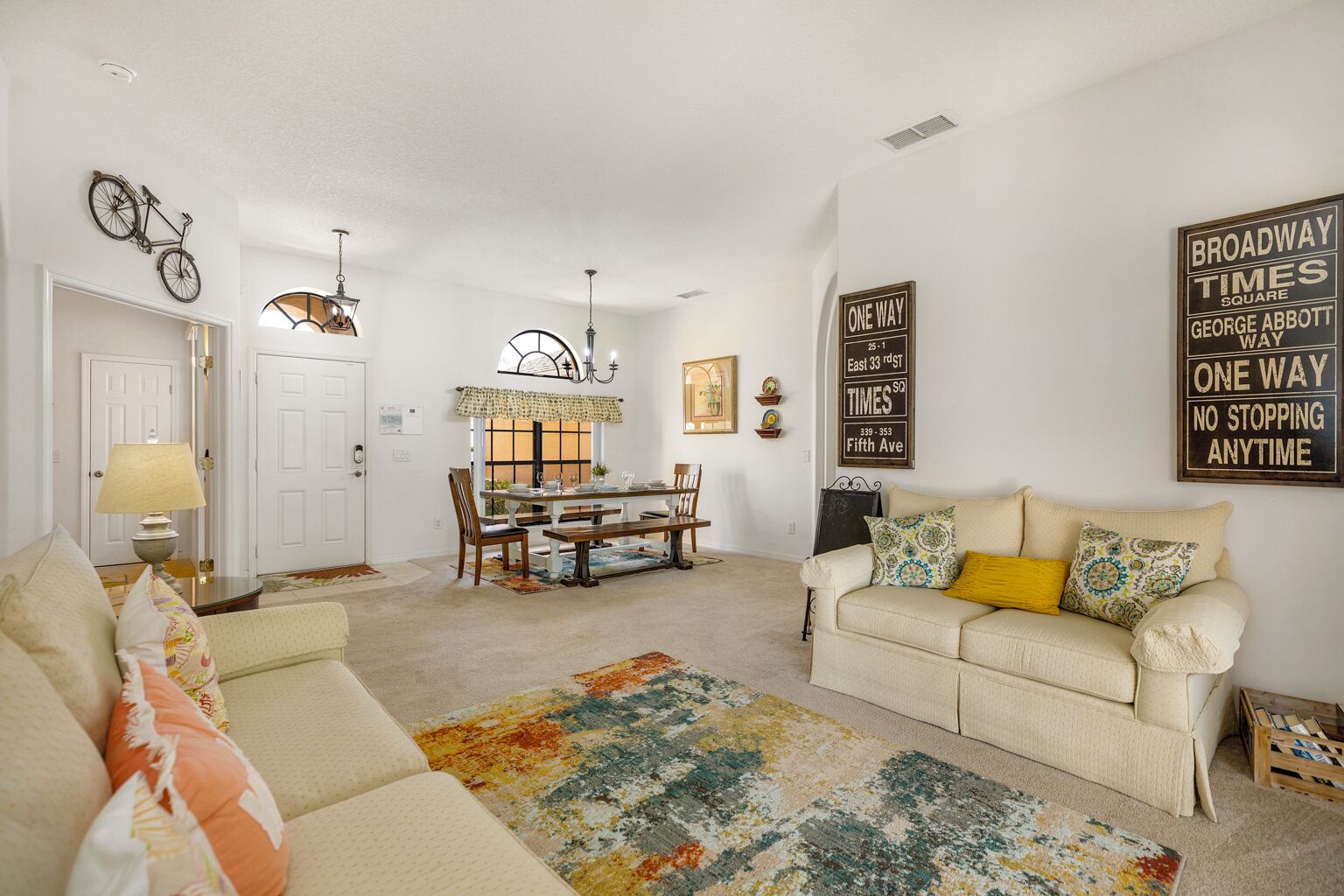 A living room with a sofa, a dining table, and a coffee table. There are decorative items on the walls and a lamp on a side table.