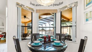 A dining area with a glass table, blue chairs, and a view of a pool through large windows. - Bahama Sunset 5 Bedrooms (Davenport)