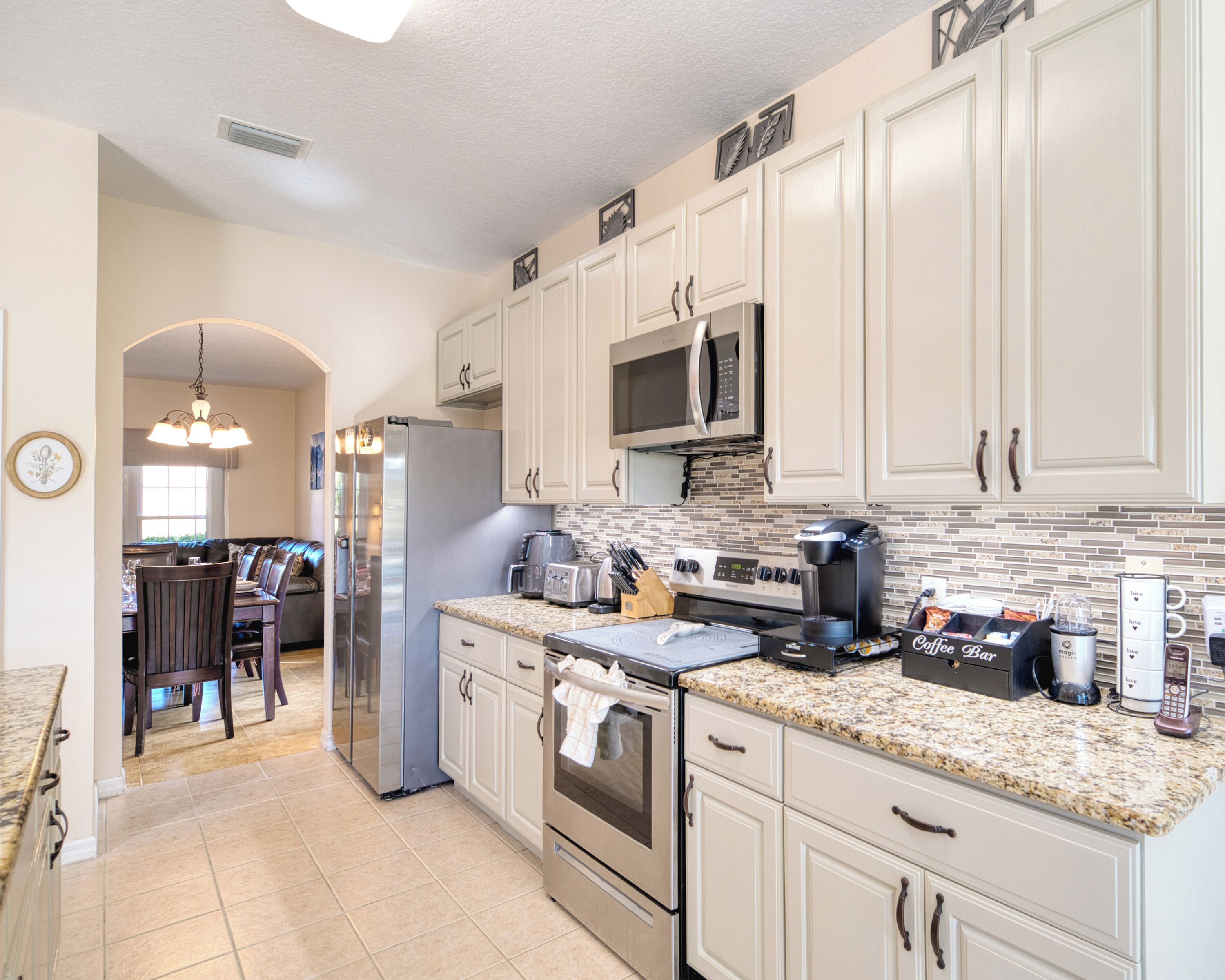 A modern kitchen with white cabinets, a granite countertop, stainless steel appliances, and a dining area with a bench.