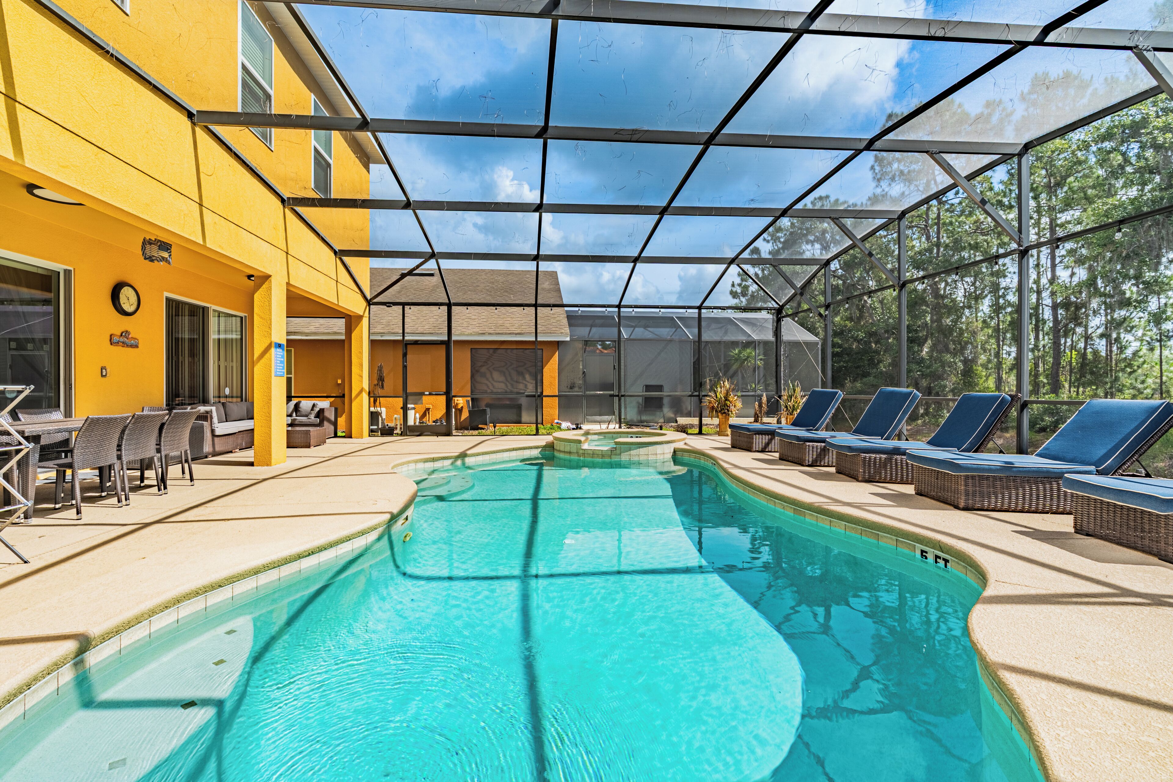 A covered swimming pool with lounge chairs, a yellow building, and a clear sky.