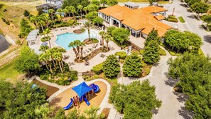 An aerial view of a resort with a swimming pool, a children's play area, and a large building with a tiled roof.
