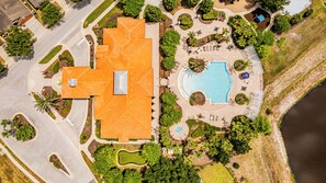 An aerial view of a resort with a large swimming pool, a tennis court, and a well-maintained garden.