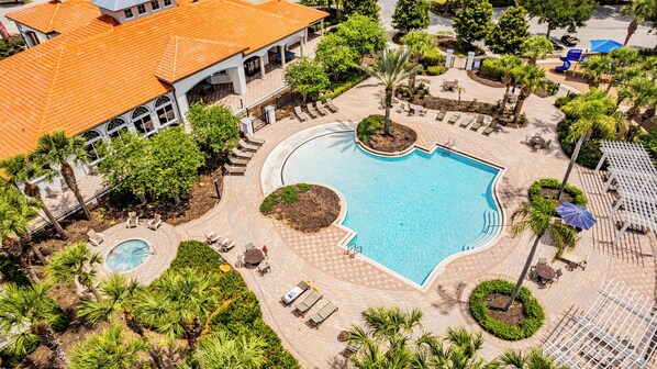 A resort with a central swimming pool, lounge areas, and a building with a tiled roof.