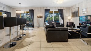 A modern living room with a sofa, a coffee table, a TV, and a bar area with stools. - Blissful Retreat 6 Bedrooms (Davenport)