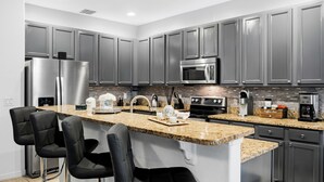 A modern kitchen with stainless steel appliances, granite countertops, and bar stools. - Blissful Retreat 6 Bedrooms (Davenport)